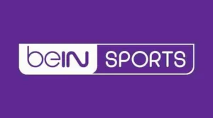 Official logo of beIN Sports: A bold, black hexagon with the orange text 'beIN' and grey text 'Sports' written in uppercase letters inside. The hexagon is enclosed by a white, curved-triangle shape with an orange outline